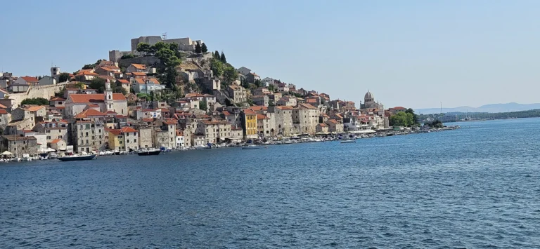 Šibenik’s stone old town rises above the waterfront, with a hilltop fortress, cathedral dome and boats in the harbour.