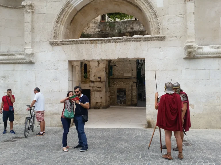 A carved stone archway in Split old town, with visitors and people dressed as Roman soldiers.