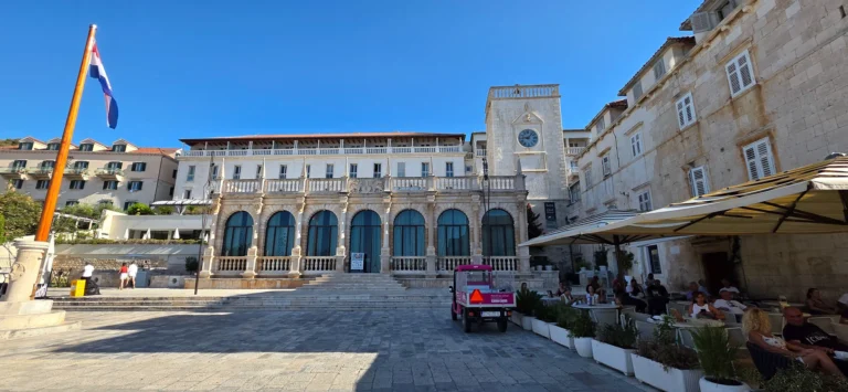 The historic town hall and clock tower on People's Square in Split, with a Croatian flag and café seating.