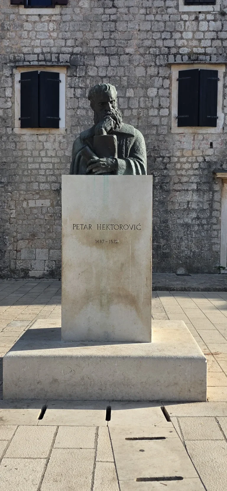 Statue of Petar Hektorović in Stari Grad, set against a pale stone building.