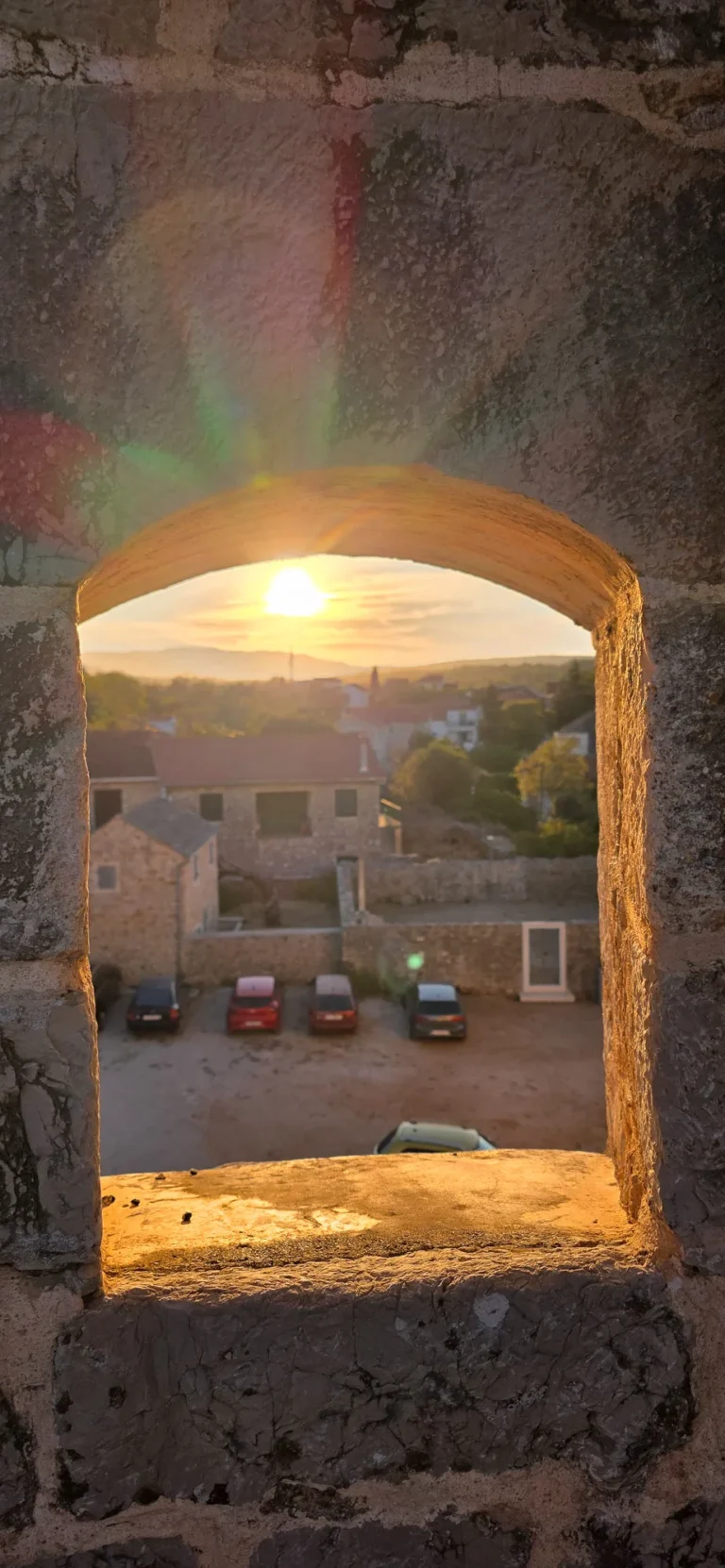 Sunset over a stone village, framed by an old stone arch.