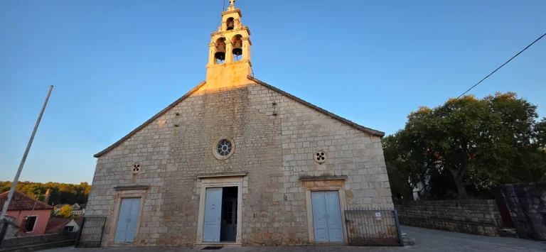 Stone church with a bell tower and three blue entrance doors beneath a clear sky