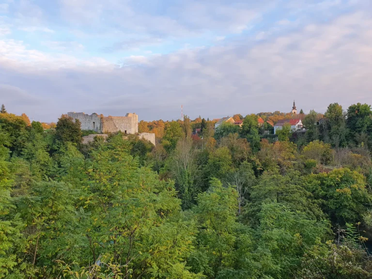 Stone fortress ruins and a distant church tower above an autumn-coloured wooded valley.