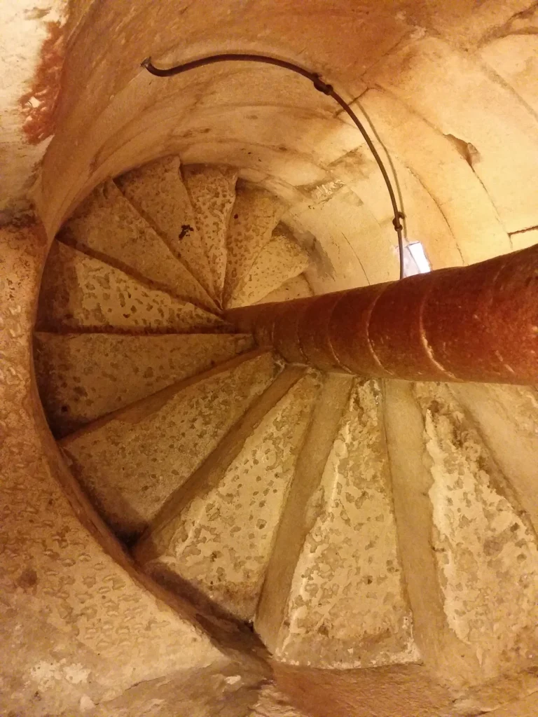 Worn stone steps spiral around a central pillar inside a warmly lit interior.