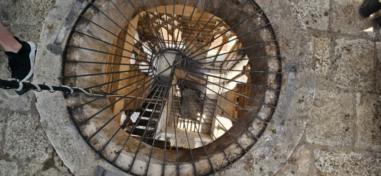 Overhead view into a circular stone stairwell with a dark iron railing