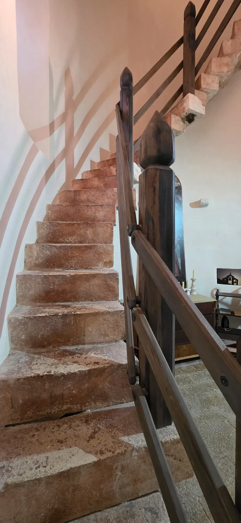 Worn stone steps rise beside a dark wooden railing in a white-walled interior.
