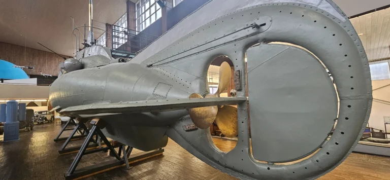 A large grey submarine on display indoors, with its stern and bronze propeller in the foreground.
