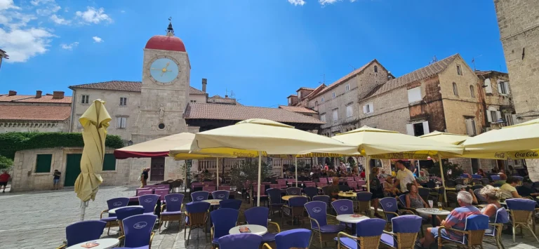 Cafés fill Trogir's stone main square beneath its clock tower and historic buildings.