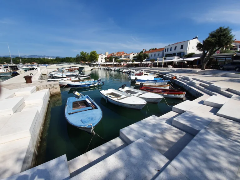 Small boats moored between pale stone quays at Umag harbour, with waterfront buildings behind them.