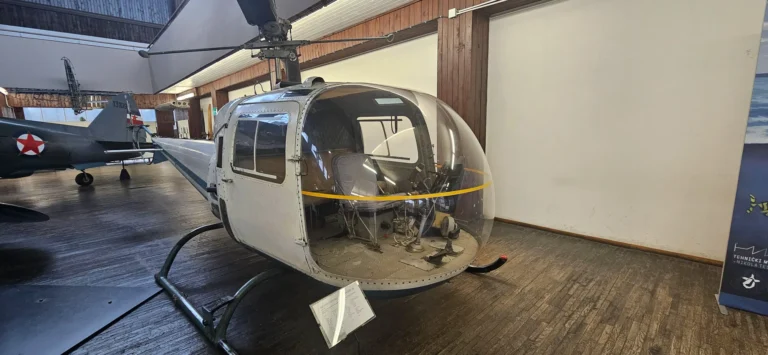 A helicopter displayed indoors at the Technical Museum Nikola Tesla in Zagreb, with another aircraft behind it.